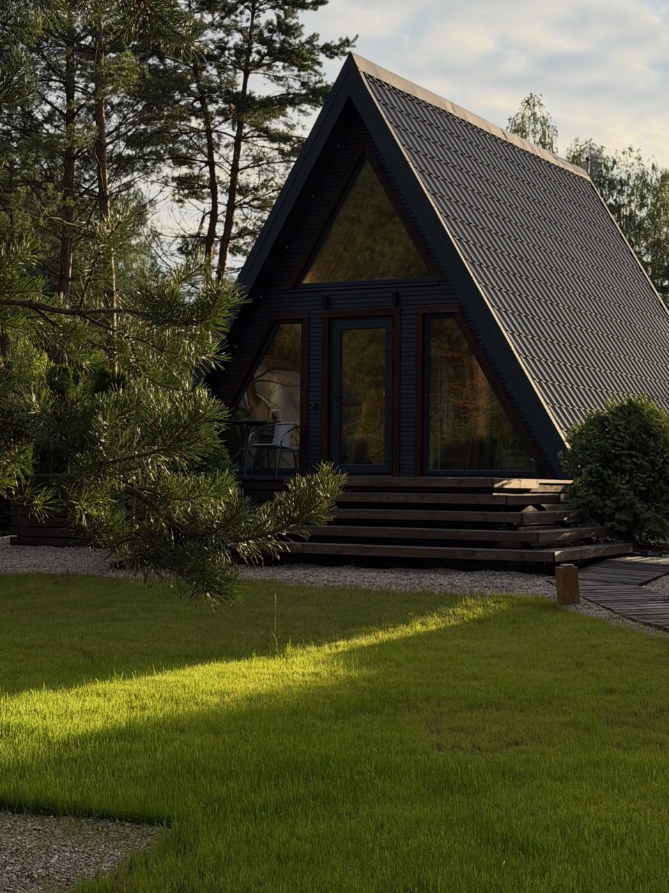 Чёрный a-frame дом среди сосен в вечернем солнце